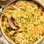 Cheese topped Philly cheesesteak skillet mixture in pan with wood spoon.