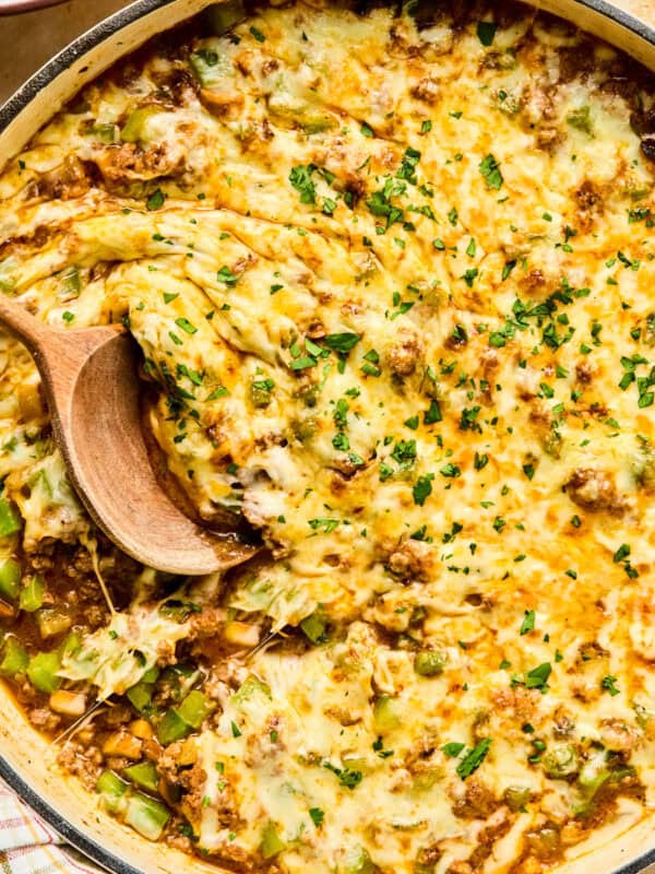 Cheese topped Philly cheesesteak skillet mixture in pan with wood spoon.