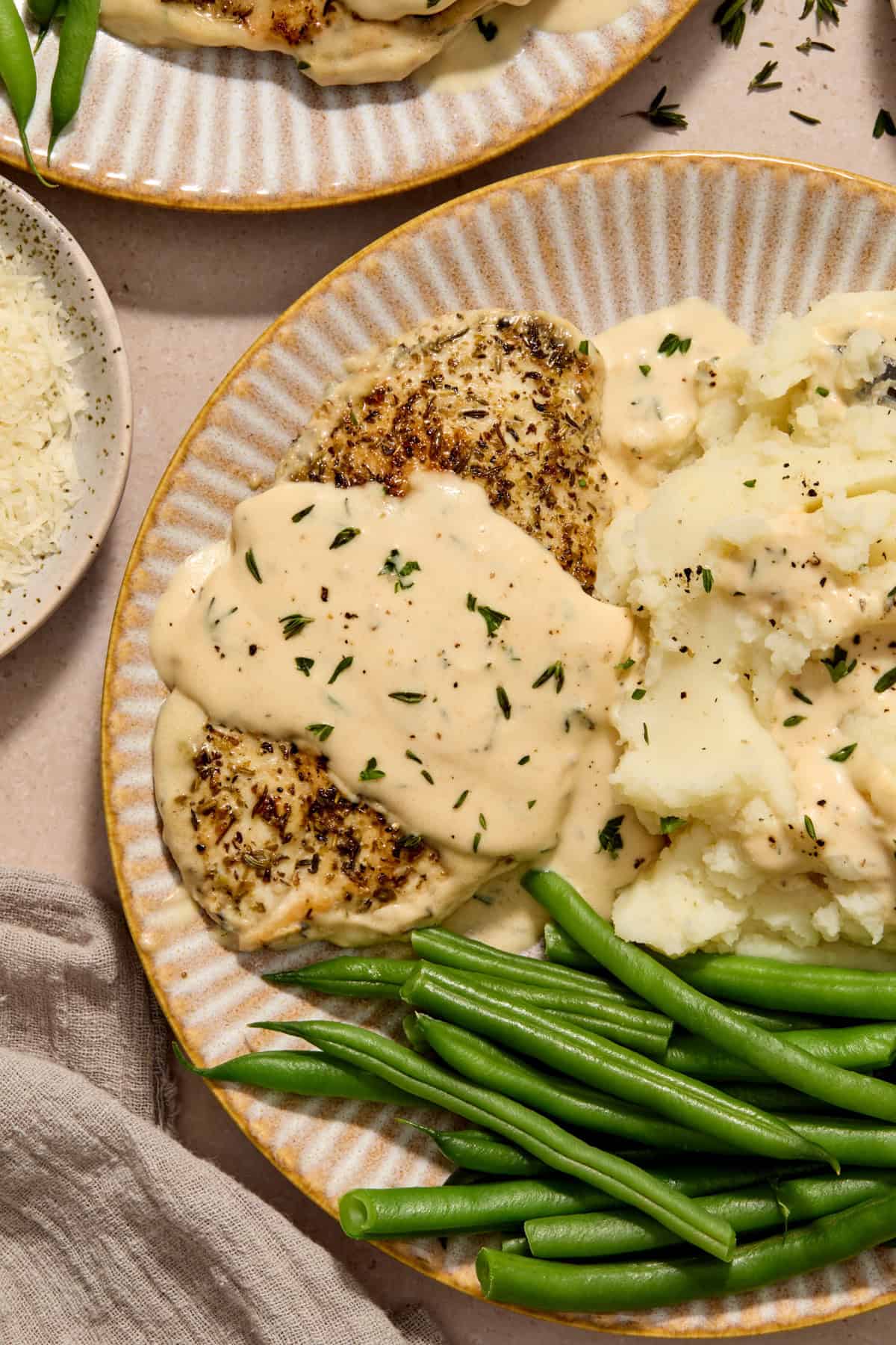 Chicken cutlet with creamy garlic parmesan over top on plate with mashed potatoes and green beans.