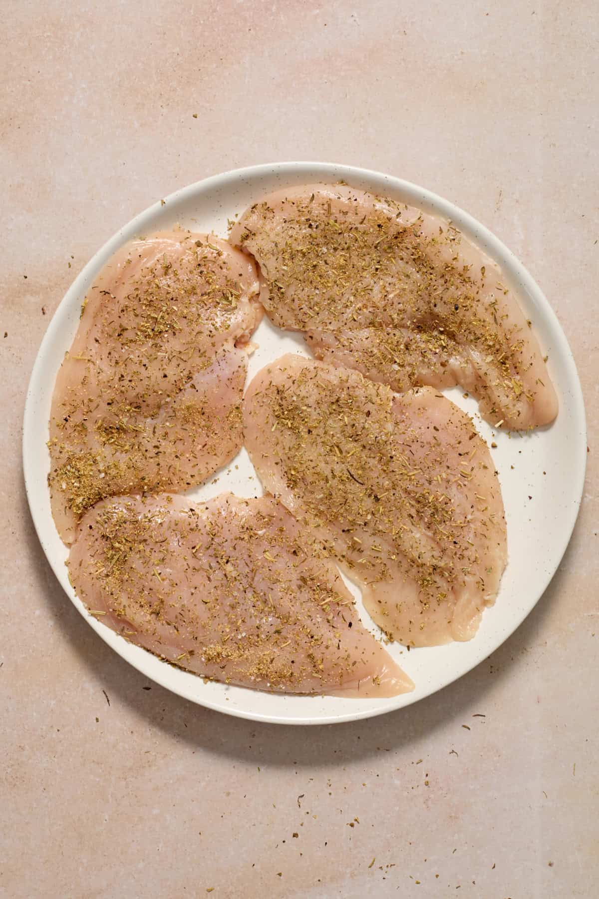 Seasoned chicken breast on plate before cooking.