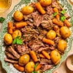 Plate with pot roast served with meat, potatoes and carrots and chopped parsley on top.