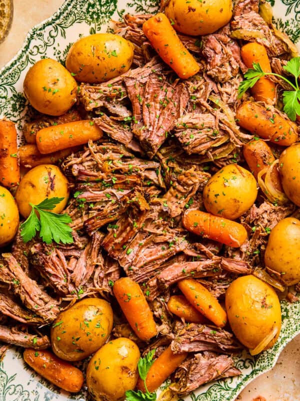 Plate with pot roast served with meat, potatoes and carrots and chopped parsley on top.