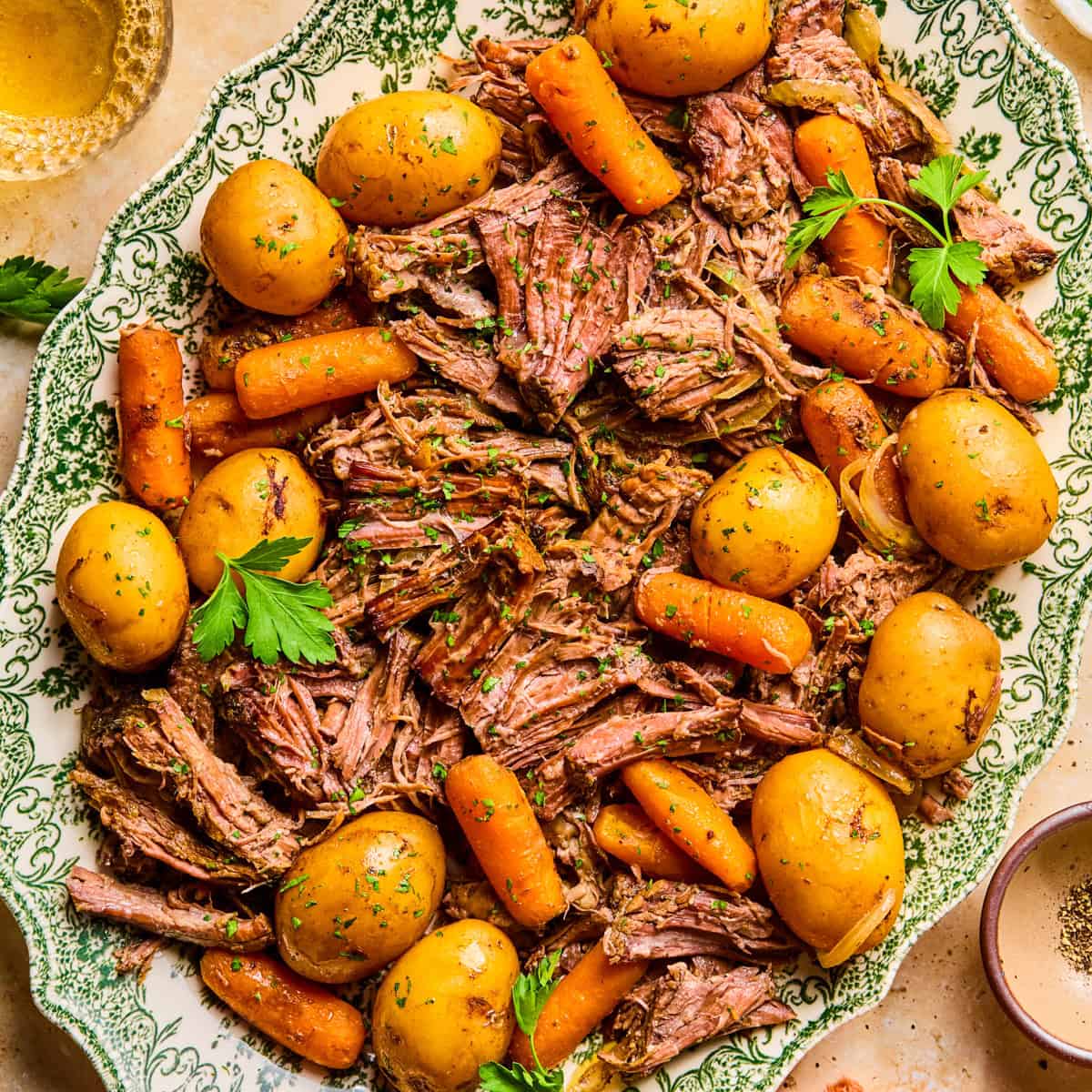 Plate with pot roast served with meat, potatoes and carrots and chopped parsley on top.