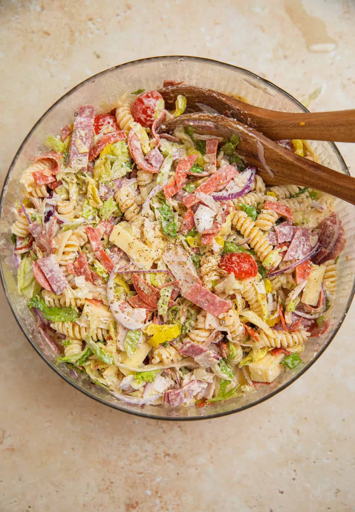 Tossed pasta salad in bowl with turkey, provolone, salami, lettuce and other ingredients.