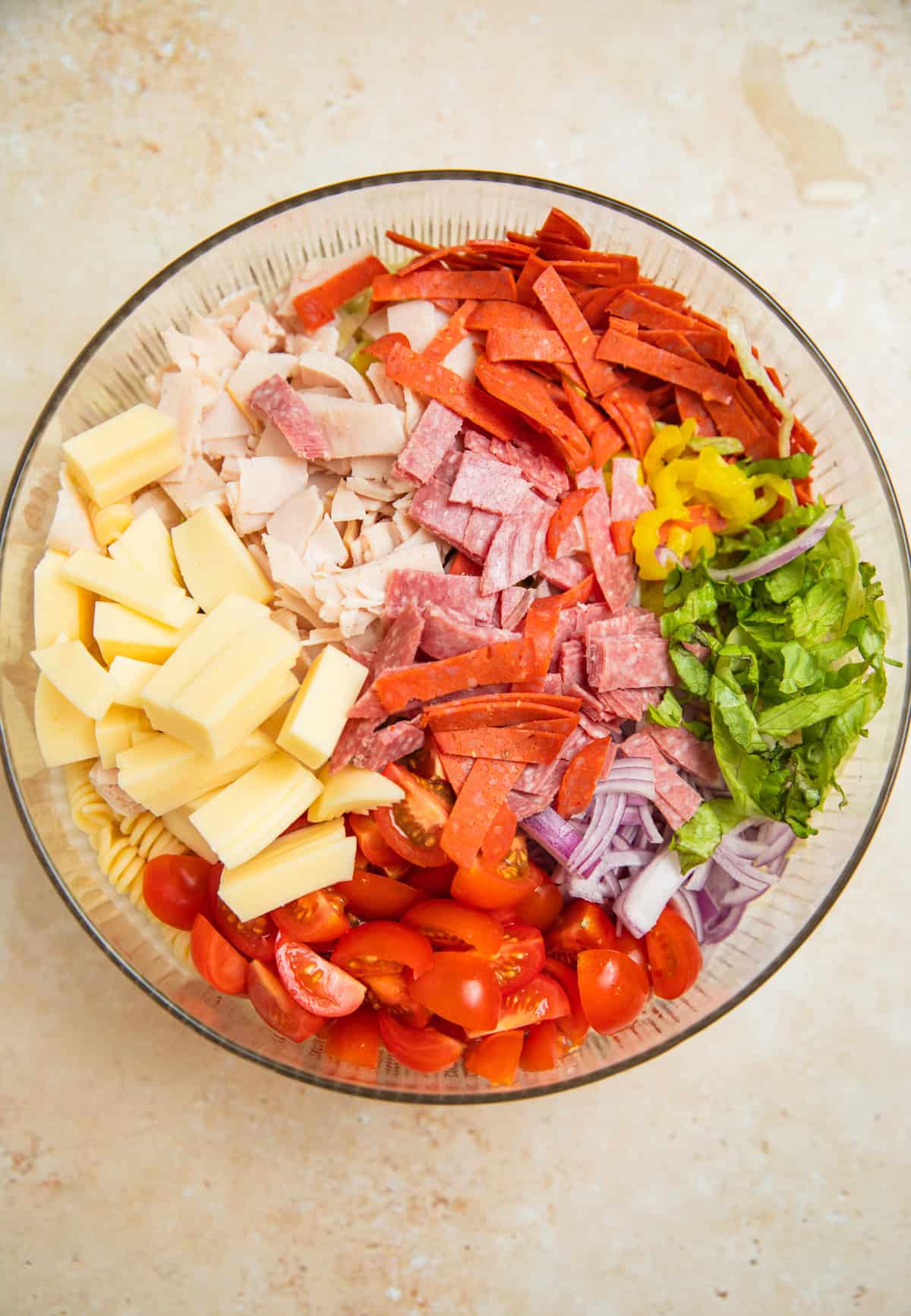 Pasta, lettuce, banana peppers, provolone and other pasta salad ingredients in bowl.