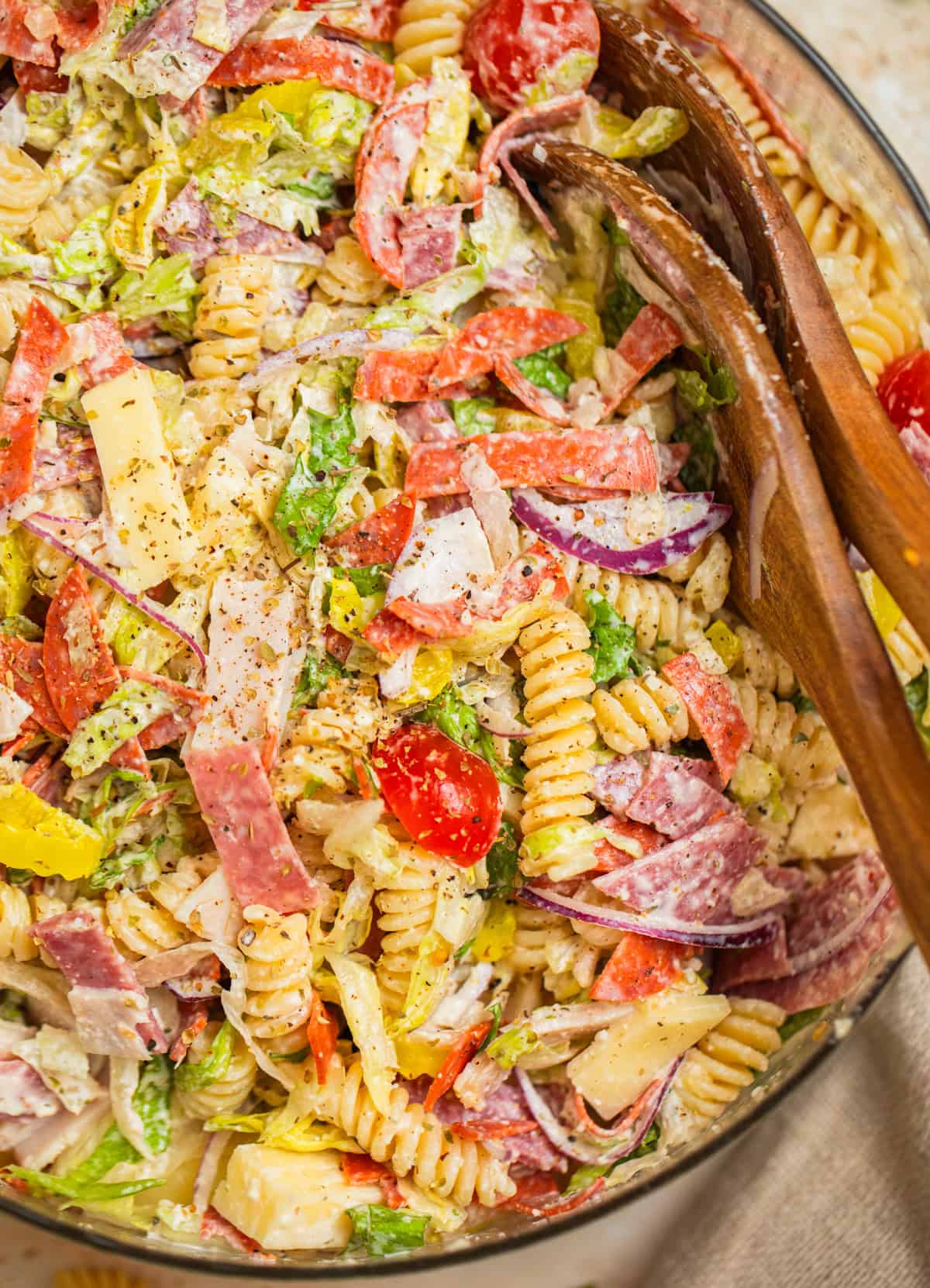 Bowl with grinder pasta salad and serving utensils propped in the bowl.