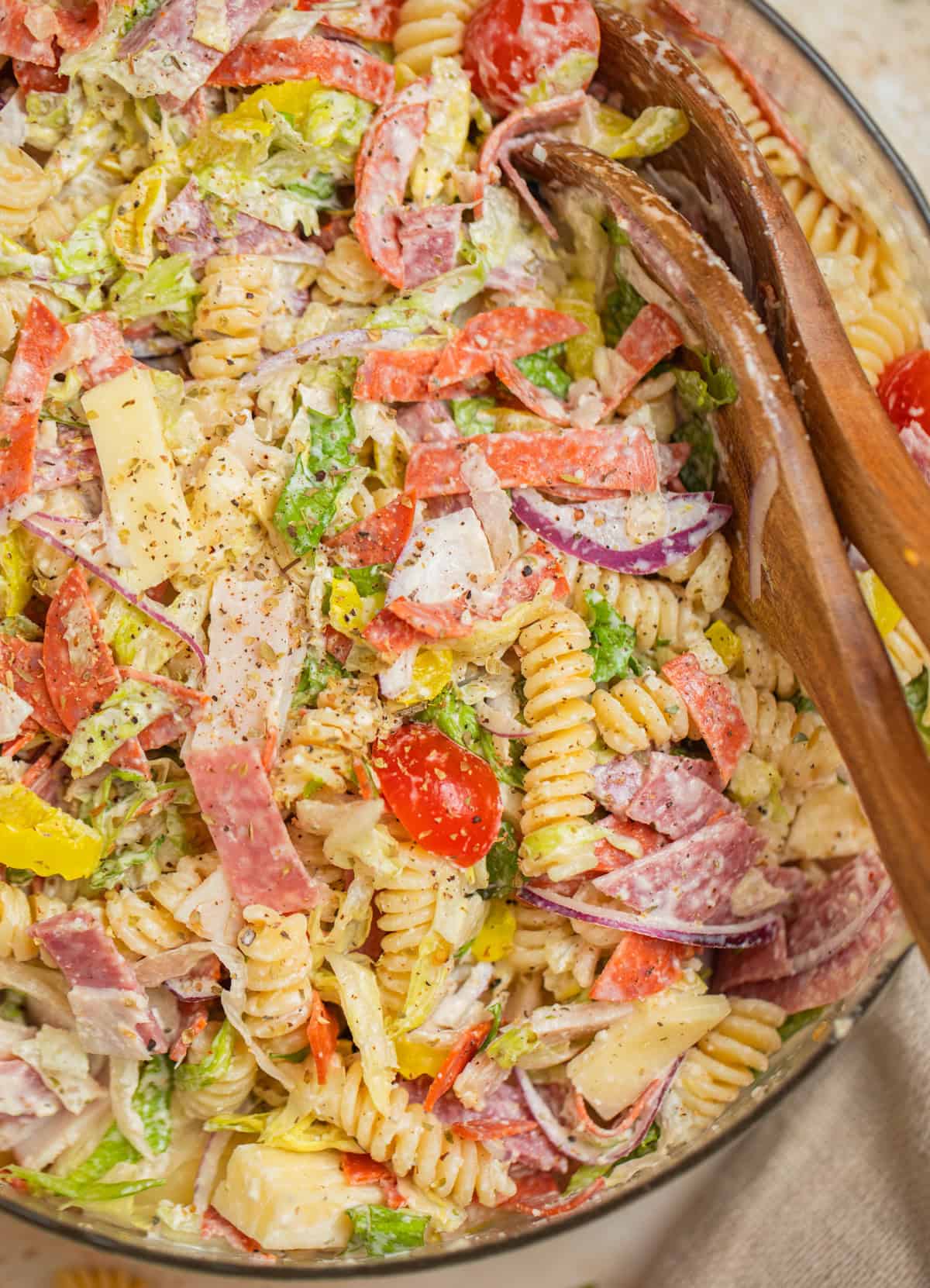 Bowl with grinder pasta salad and serving utensils propped in the bowl.