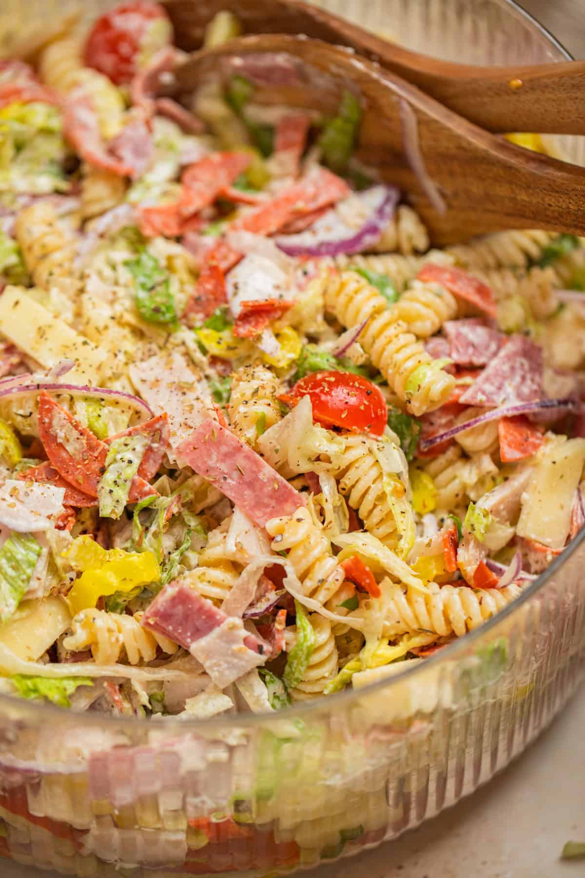 Bowl with grinder pasta salad and serving utensils propped in the bowl.