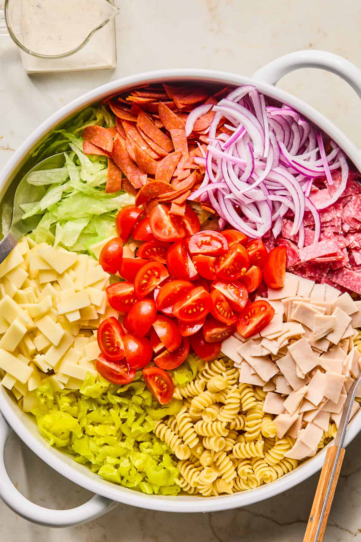 Pasta, lettuce, banana peppers, provolone and other pasta salad ingredients in bowl.