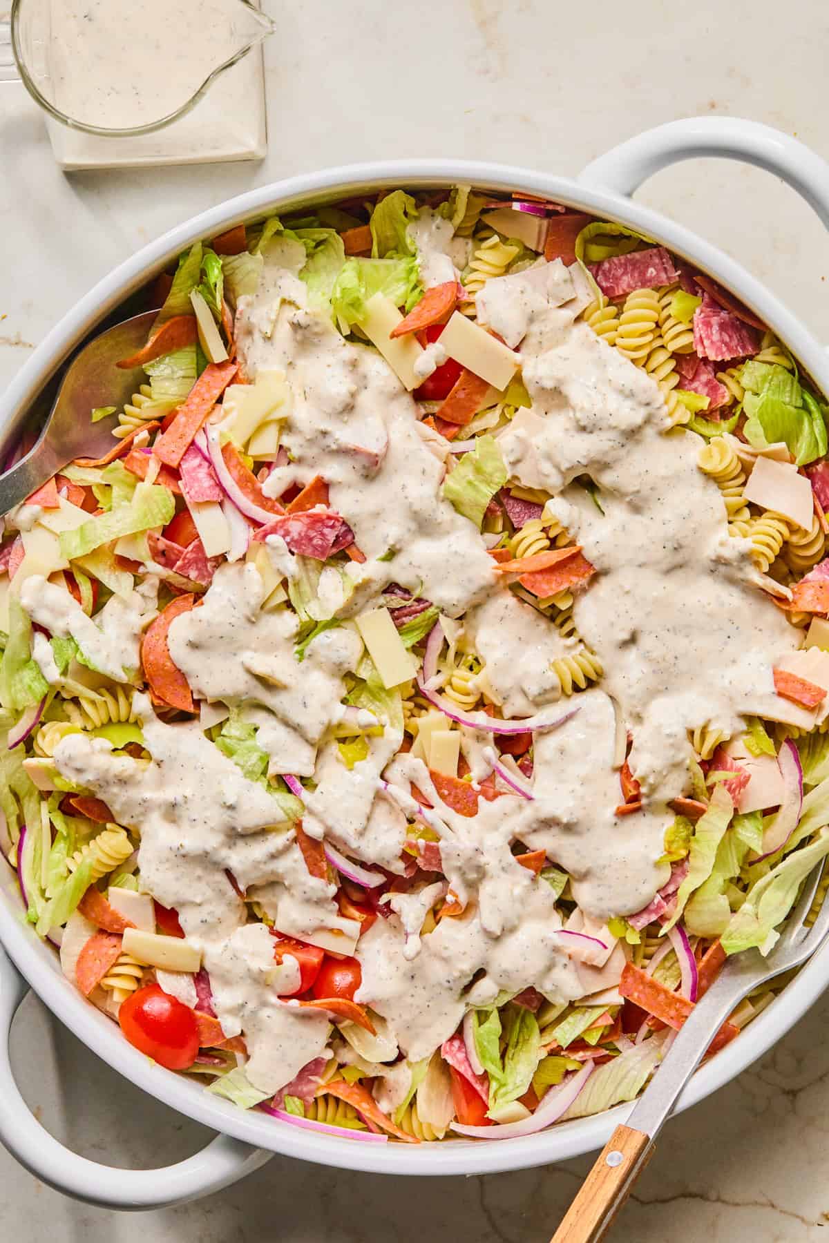 Grinder pasta salad in bowl with dressing poured over top.