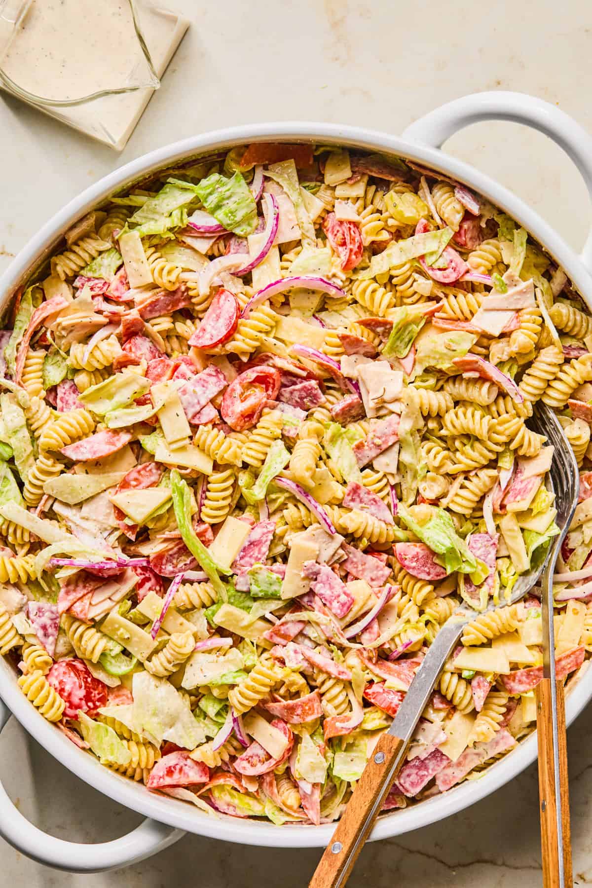 Tossed pasta salad in bowl with turkey, provolone, salami, lettuce and other ingredients.