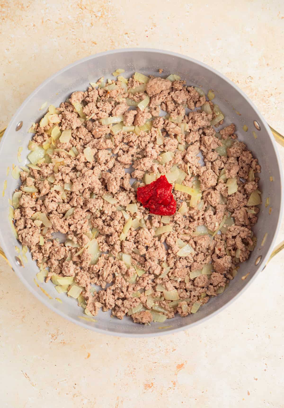 Browned ground turkey in pan with tomato paste added.