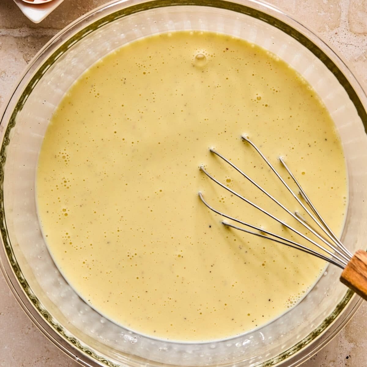Egg, milk and cream mixture in glass bowl with whisk.