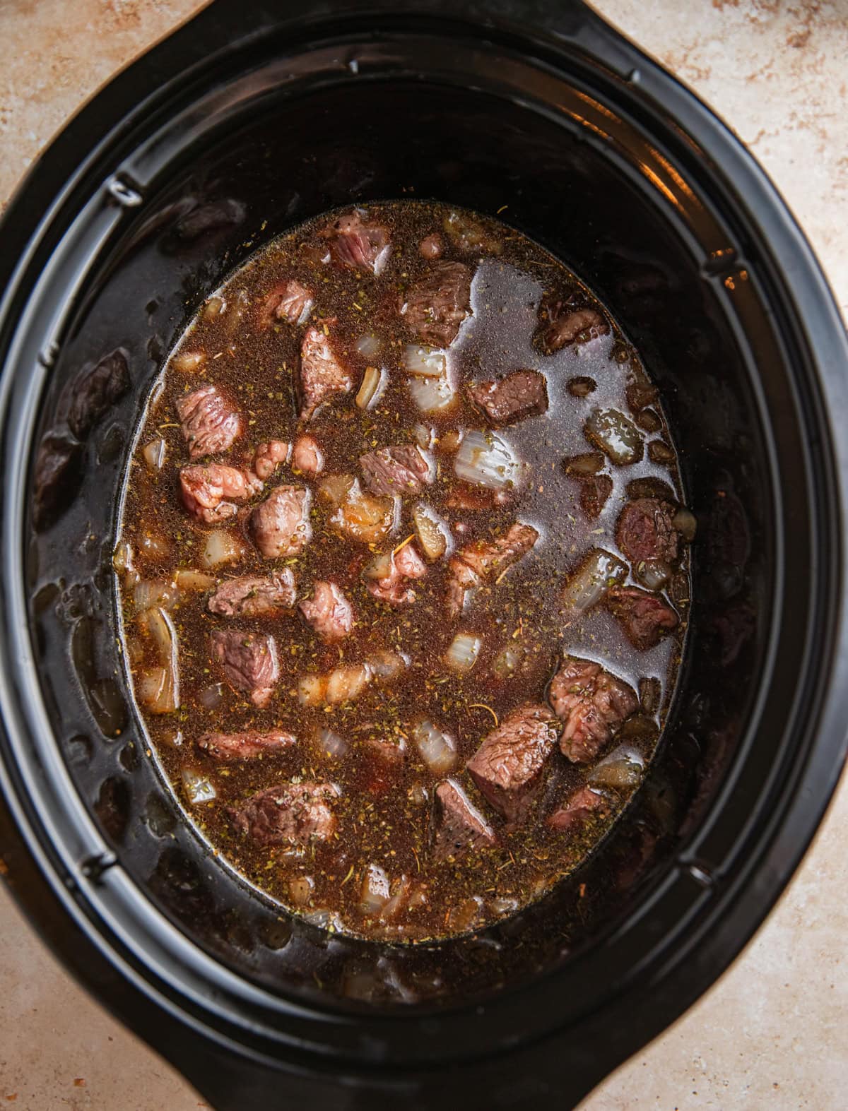 Crockpot with cubed seared beef, broth and other ingredients before slow cooking.