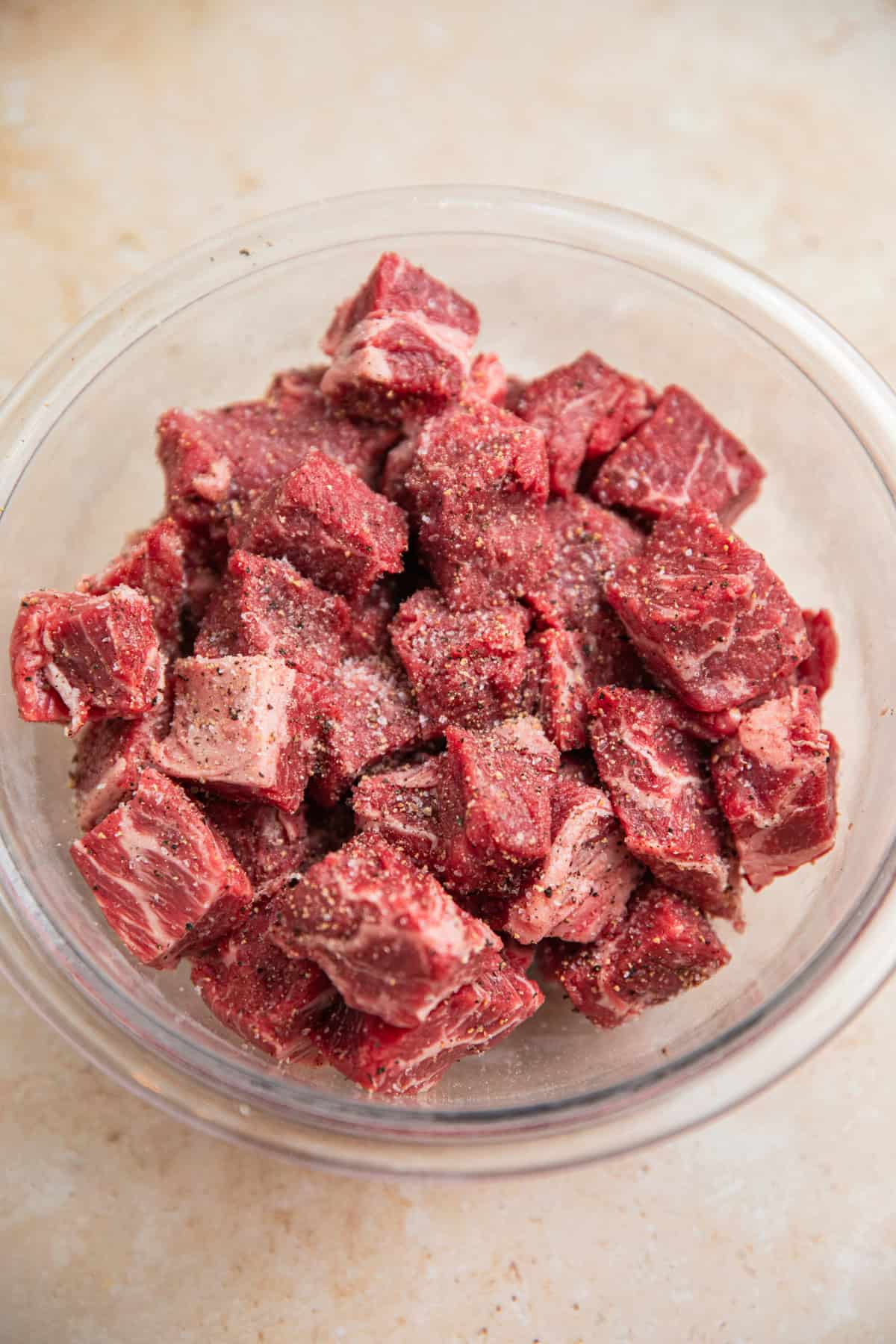 Cubed chuck roast in bowl with salt and pepper.
