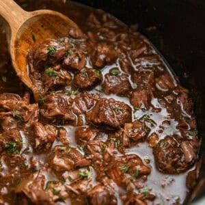 Crockpot with beef tips in gravy with wooden spoon.