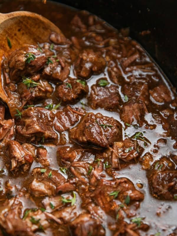 Crockpot with beef tips in gravy with wooden spoon.