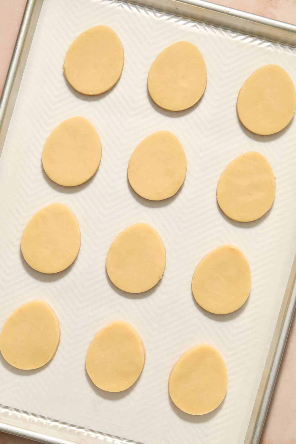 Egg shaped shortbread cookie dough cutouts on parchment lined pan.