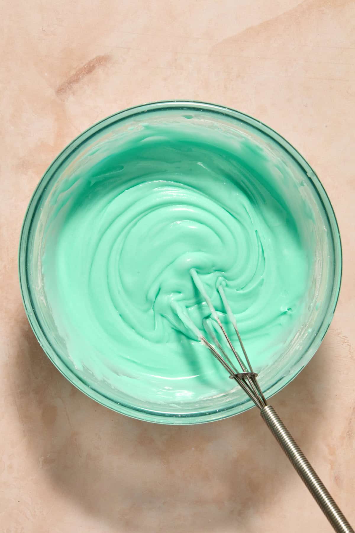 Turquoise icing with whisk in bowl.
