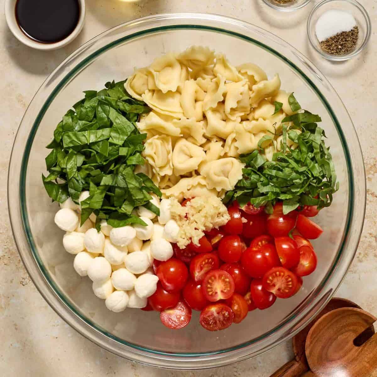Tomatoes, mozzarella, spinach and other ingredients added to pasta in mixing bowl.