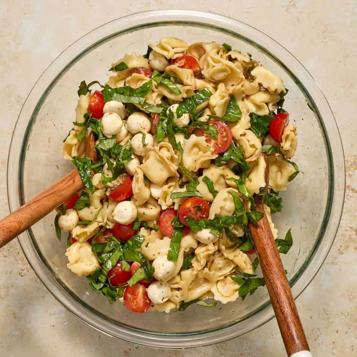 Tossed tortellini caprese pasta salad with salad tongs.