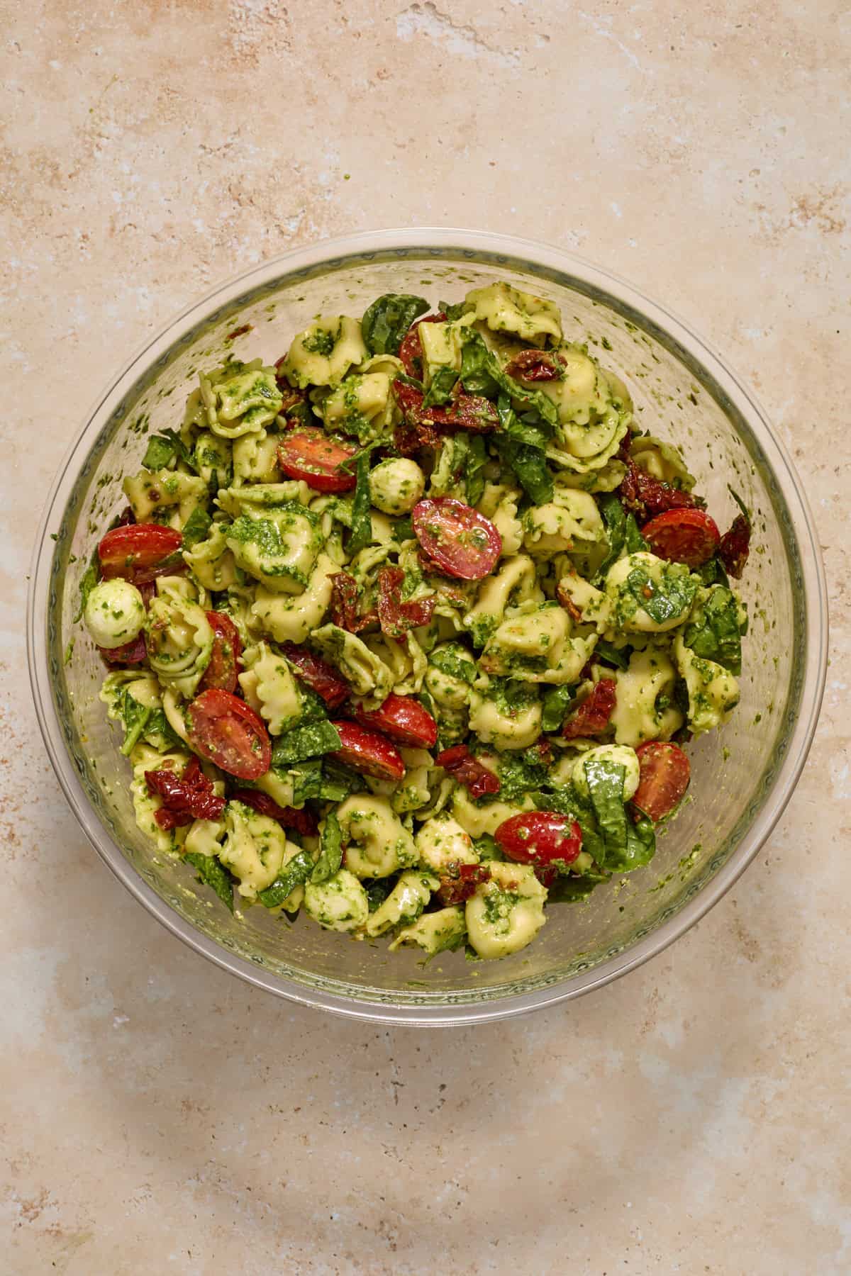 Prepared tortellini pesto pasta salad in mixing bowl.