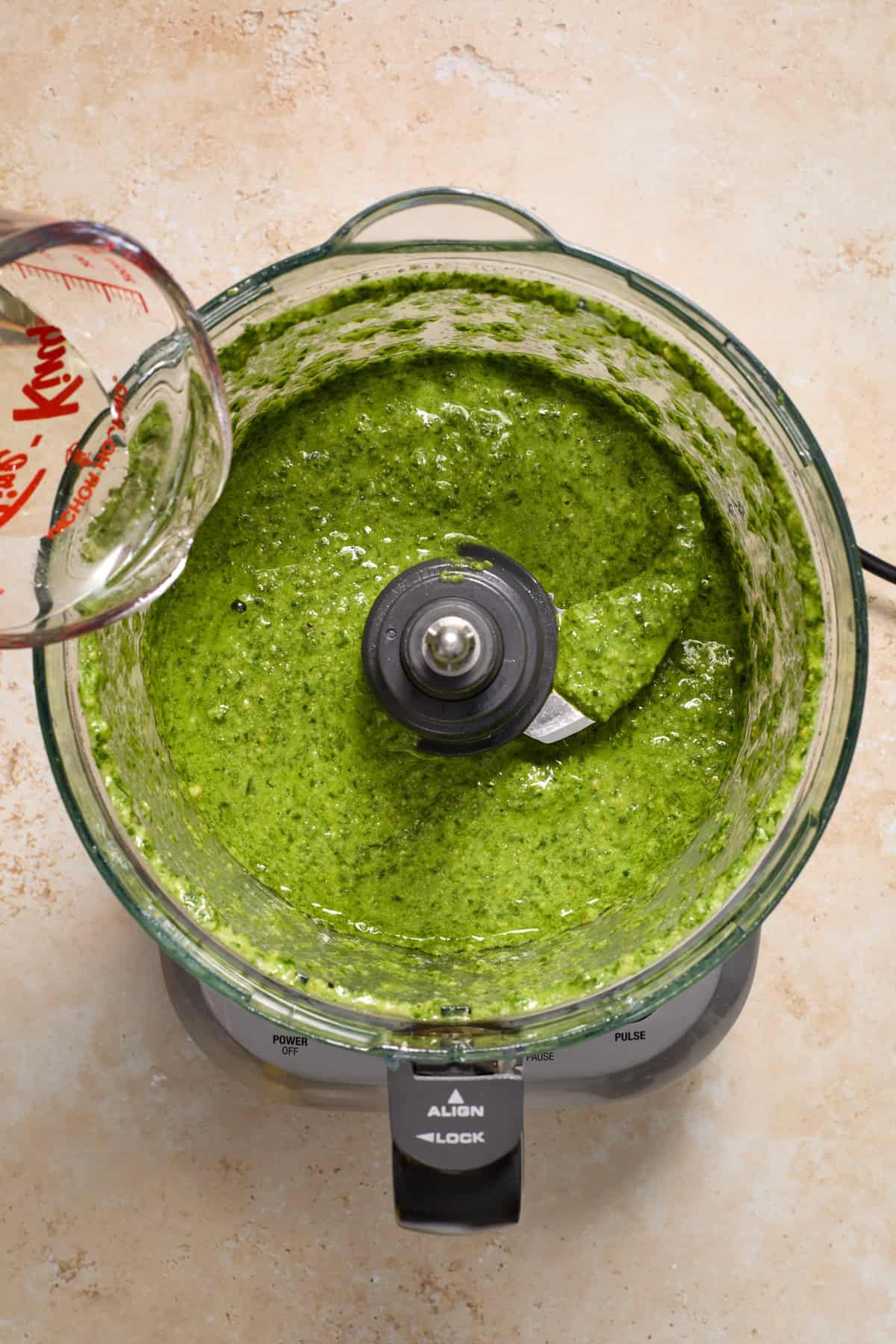 Olive oil being poured into pesto mixture in food processor.