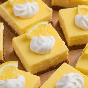 Sliced creamy lemon bars topped with dollop of whipped cream and lemon slice.