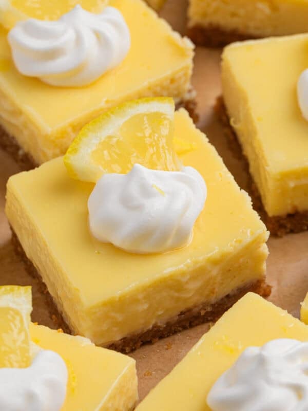 Sliced creamy lemon bars topped with dollop of whipped cream and lemon slice.