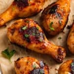 Honey mustard chicken drumsticks on parchment with chopped parsley.