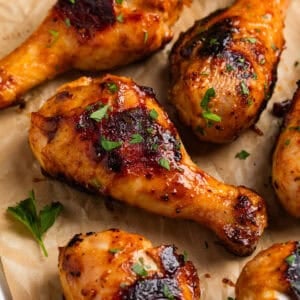 Honey mustard chicken drumsticks on parchment with chopped parsley.
