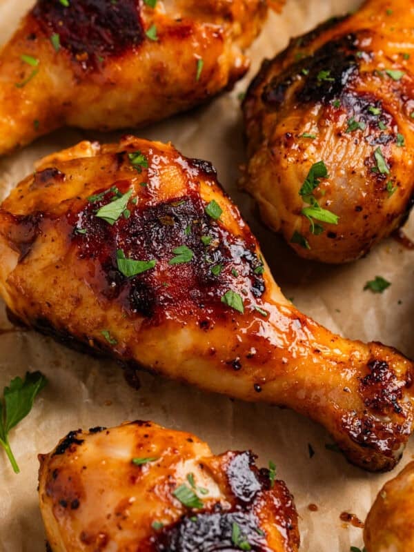 Honey mustard chicken drumsticks on parchment with chopped parsley.