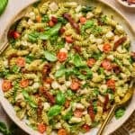 Pesto chicken pasta salad in serving bowl topped with fresh basil with serving spoon.