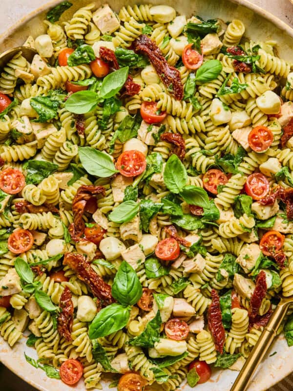 Pesto chicken pasta salad in serving bowl topped with fresh basil with serving spoon.