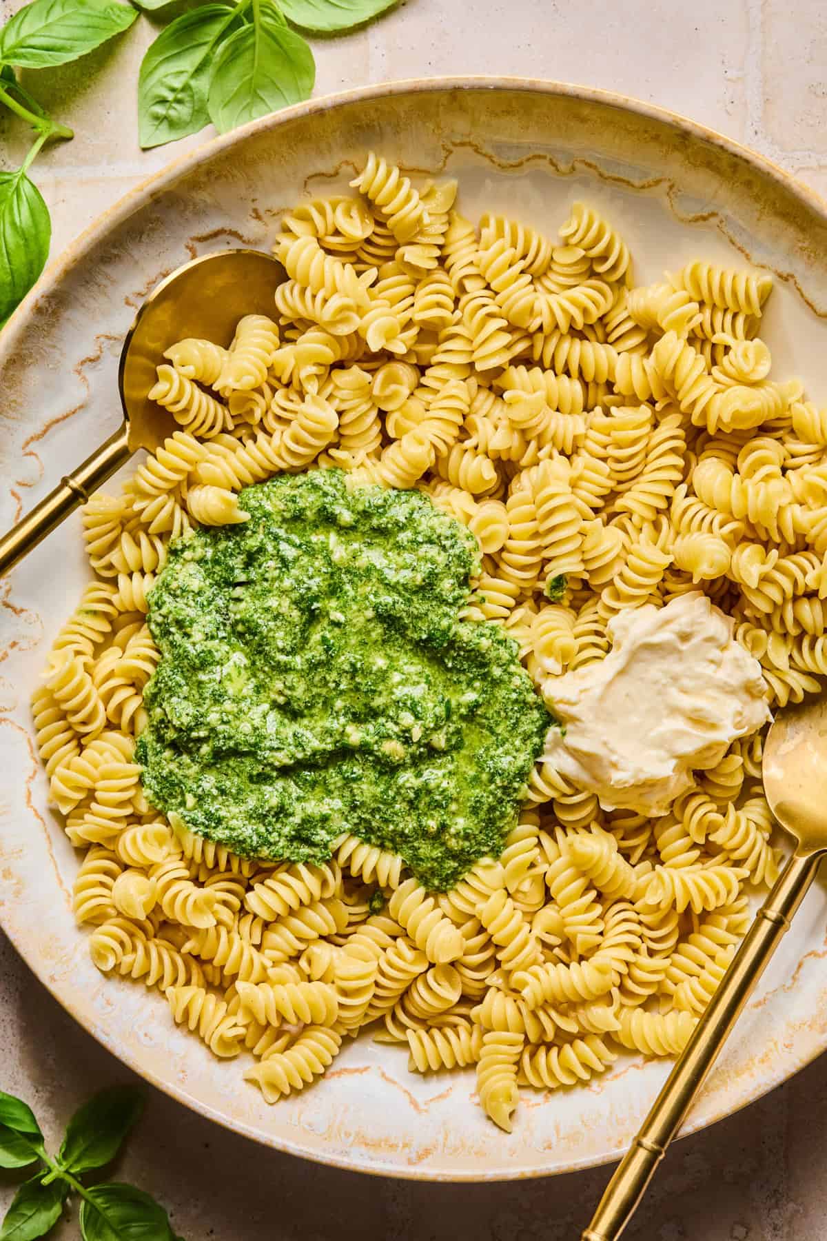 Pesto and mayo over top of pasta in bowl with spoons.