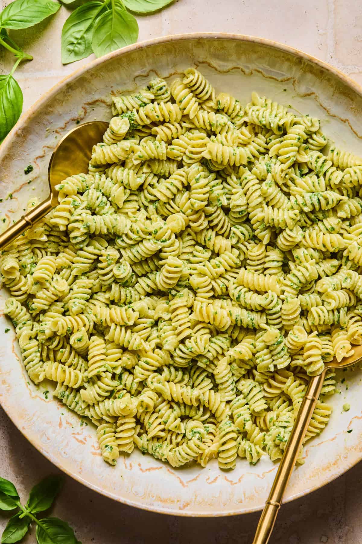 Pesto tossed with rotini pasta with utensils.