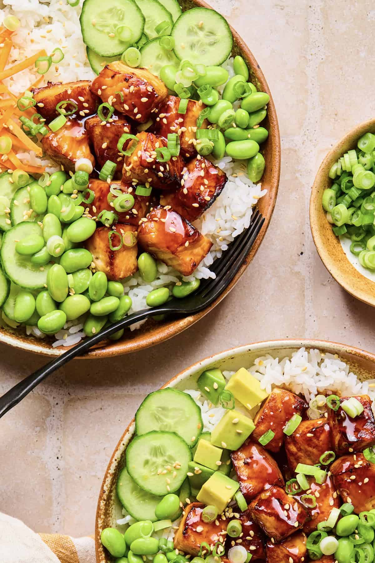 Teriyaki salmon bites in rice bowls with edamame, cucmbers and other ingredients.