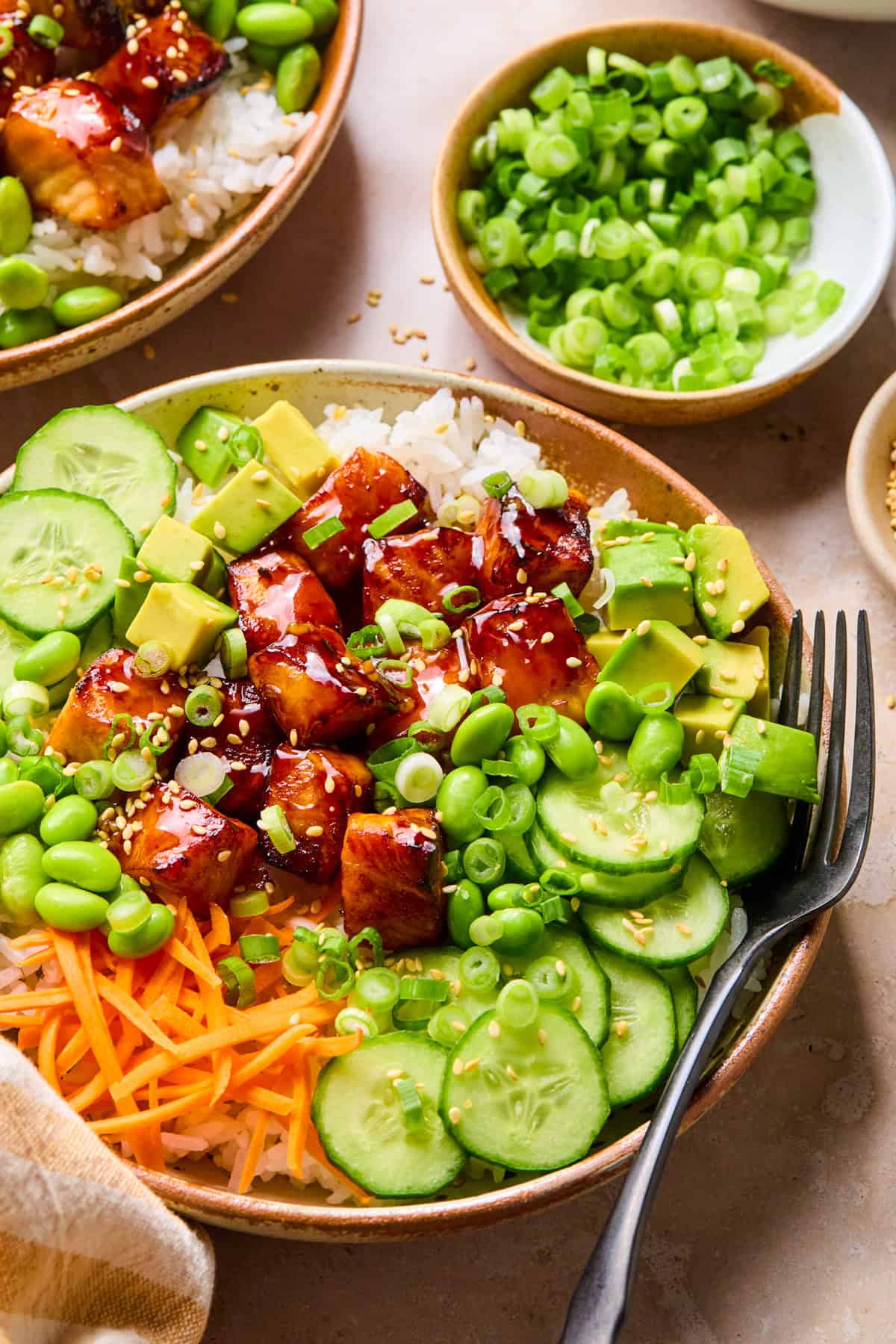 Teriyaki salmon cubes in rice bowls with cucumbers, carrots and green onion.