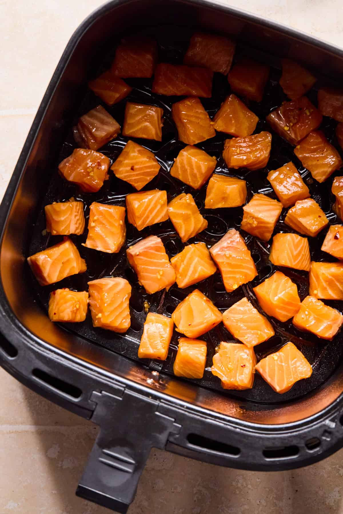 Air fryer with marinaded salmon bites before cooking.