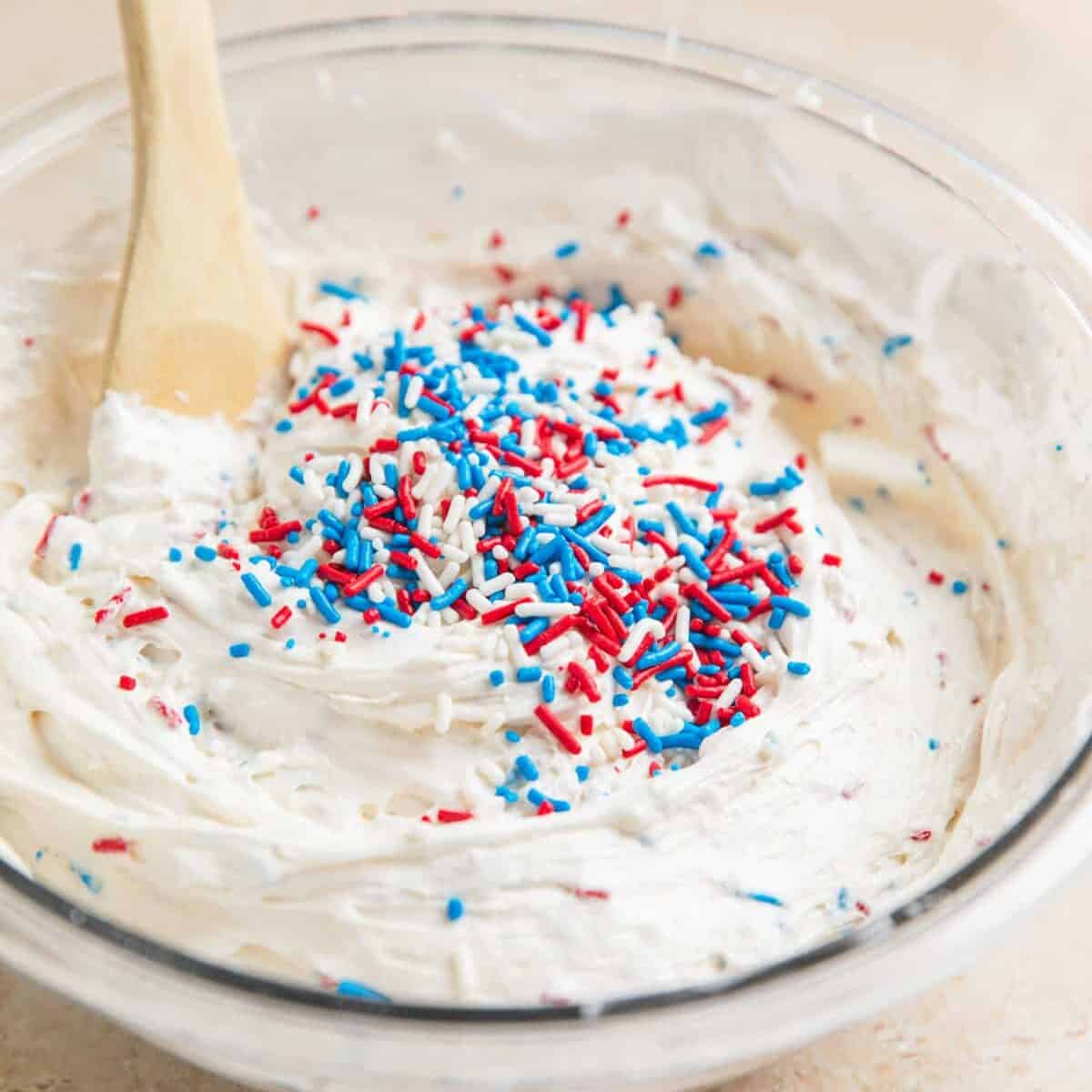 Red, white and blue sprinkles being stirred into dip.