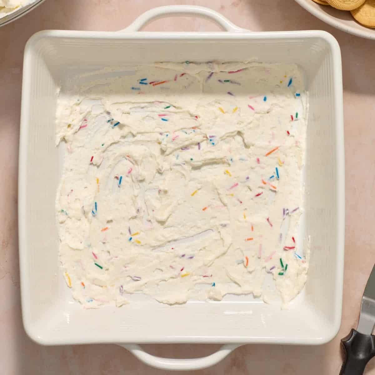 Funfetti whipped cream mixture spread on the bottom of square pan.