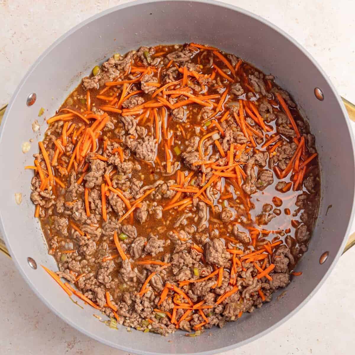 Browned ground beef with carrots and sauce added to pan.