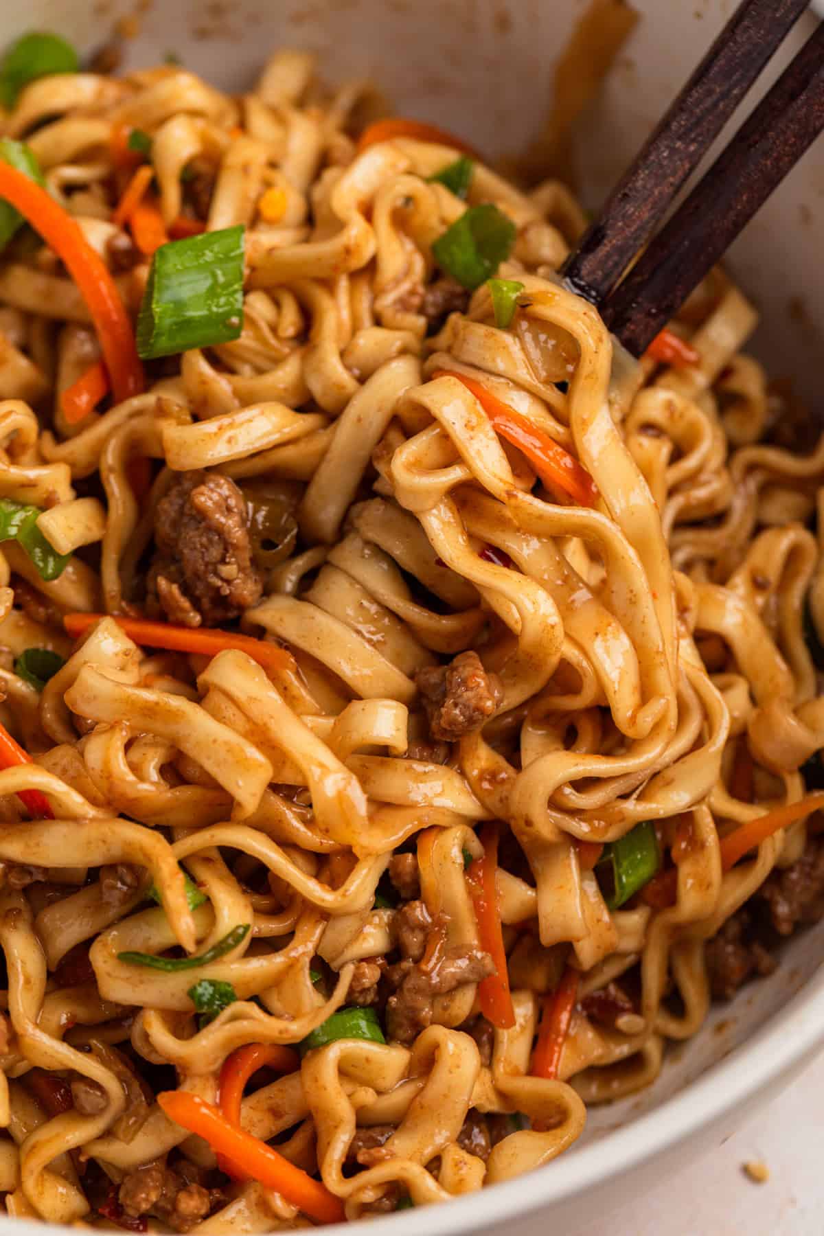 Beef noodles on chopsticks in bowl.
