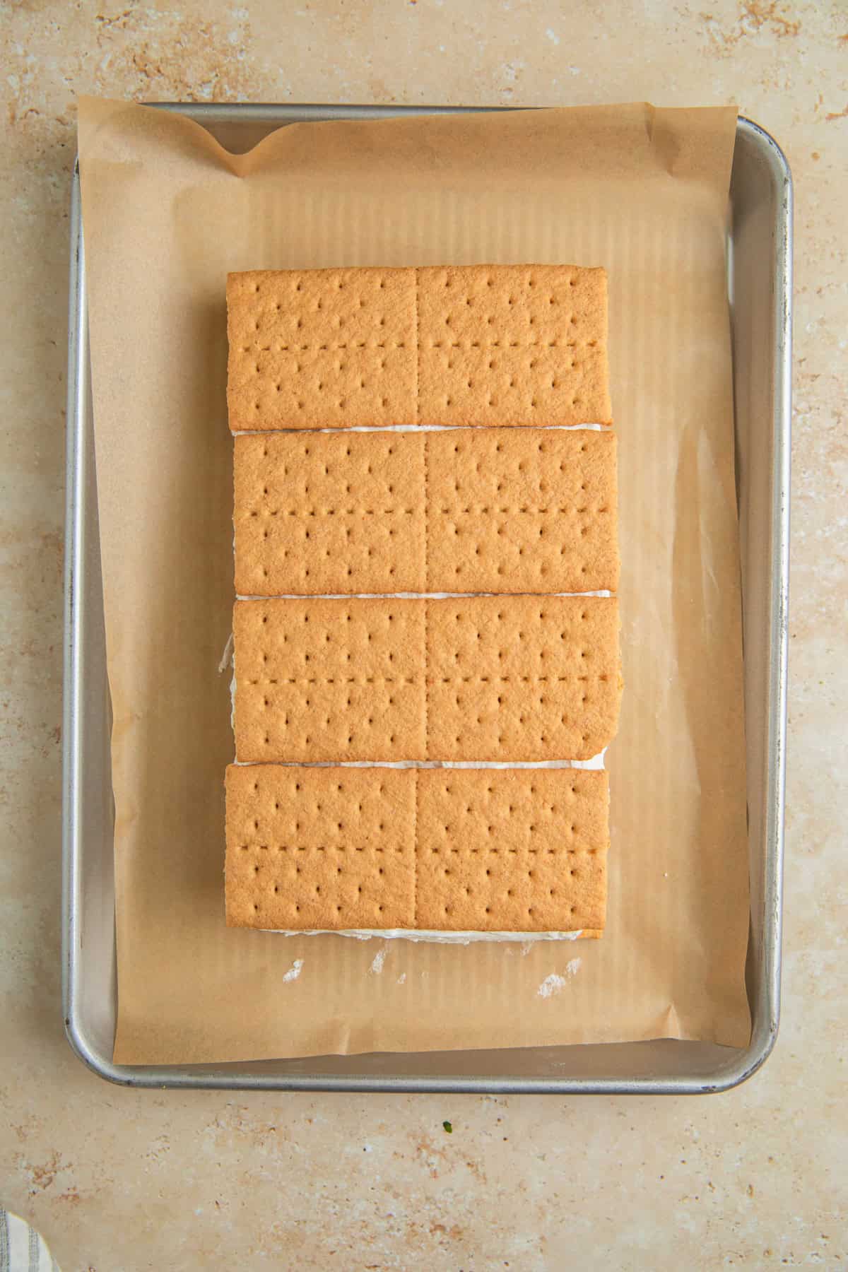 Graham crackers layered over top of lemonade whipped cream on pan with parchment.
