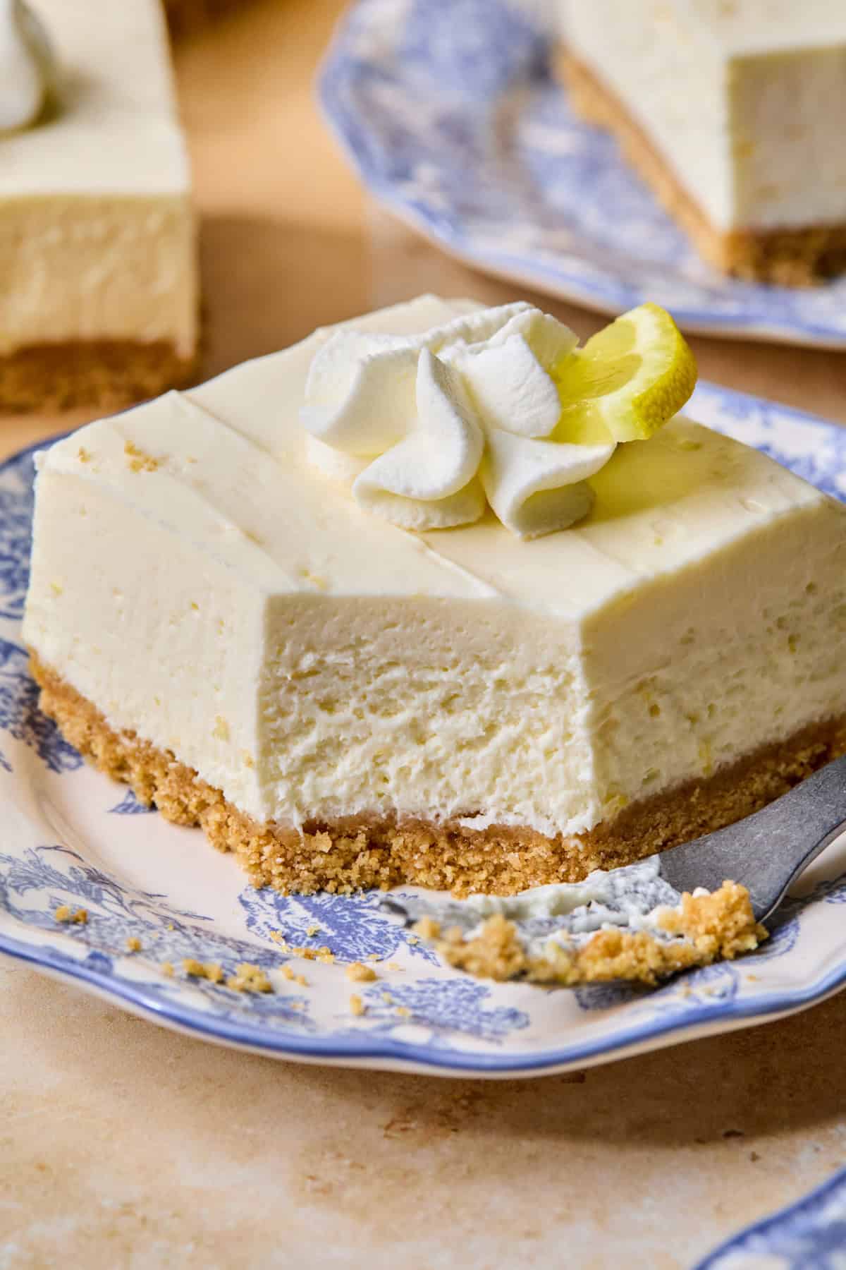 Slice of no-bake lemon cheesecake bar on plate with forkful taken out to show texture.