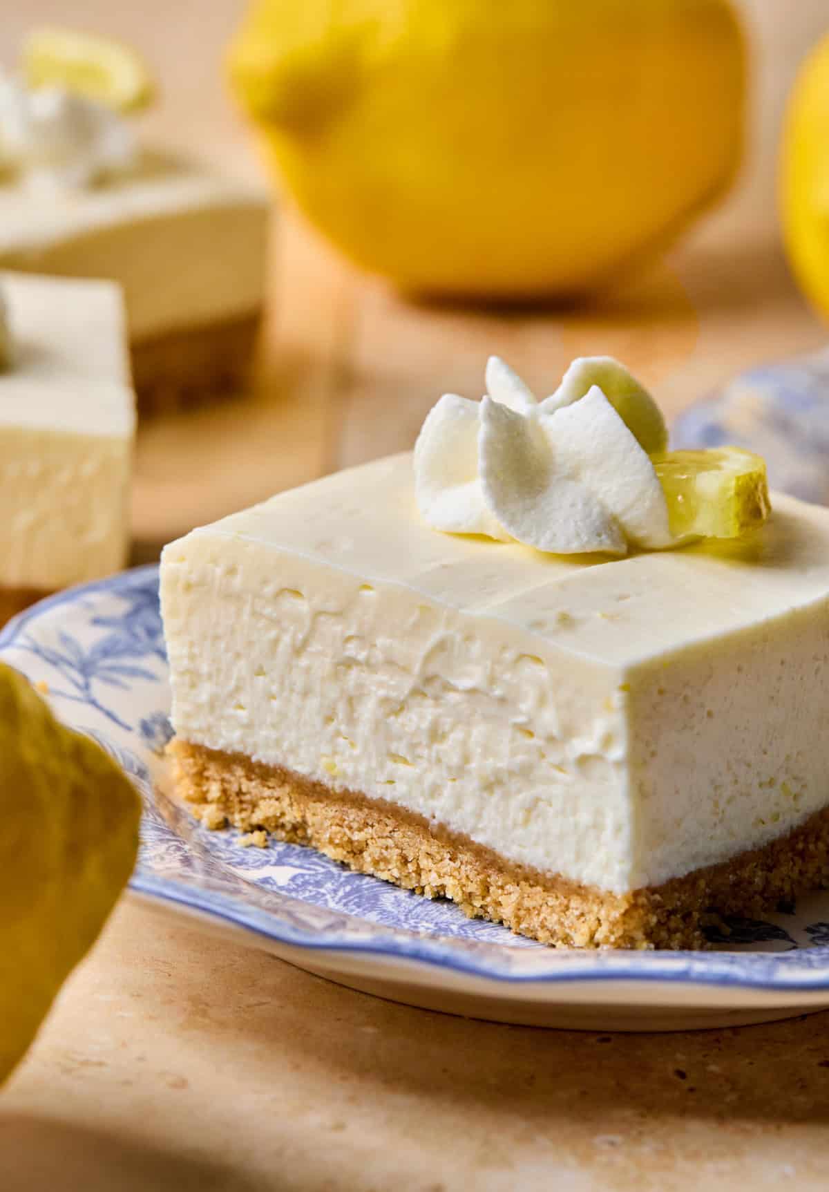 Lemon cheesecake bar on plate with whipped cream and lemon slice on top.