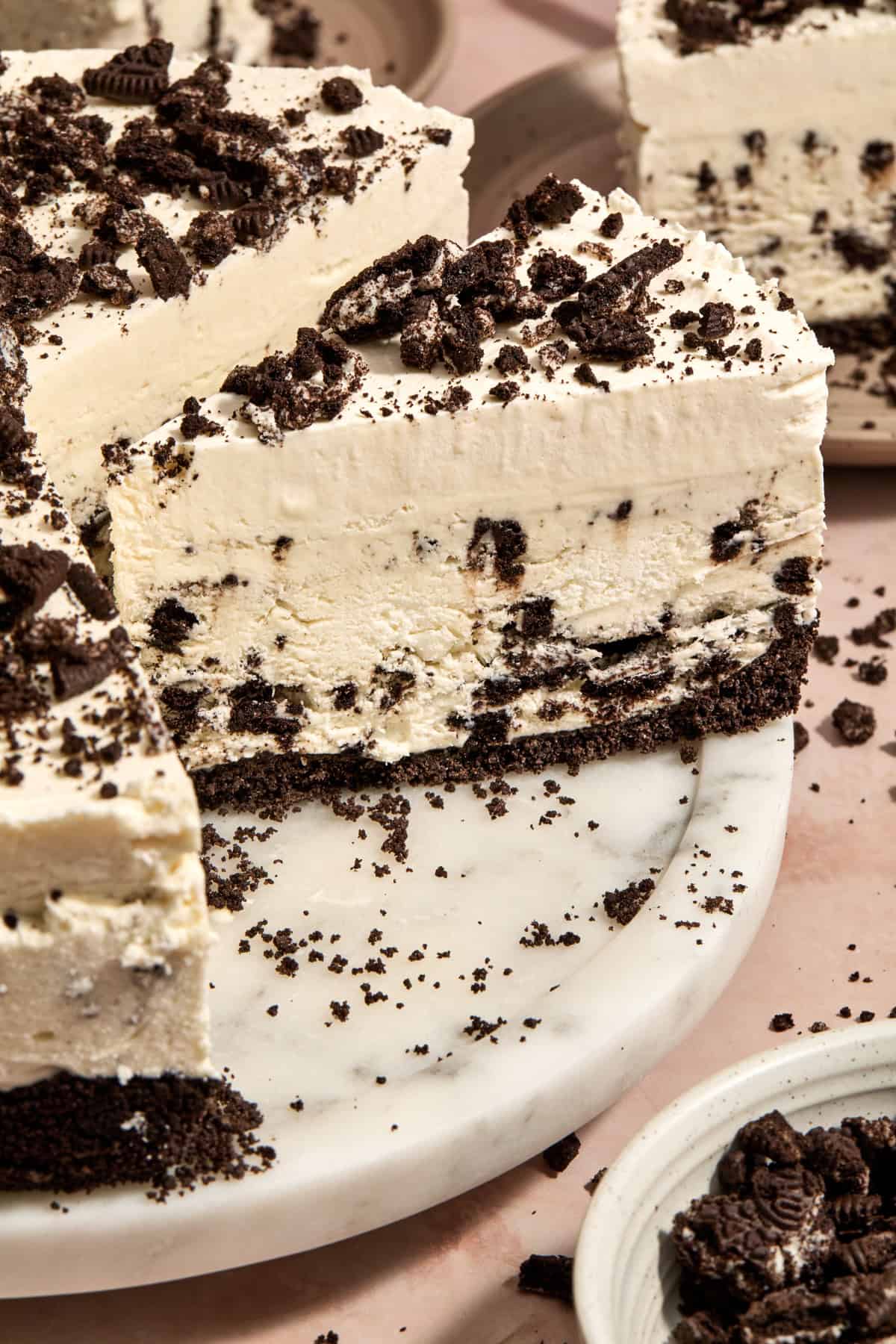 Ice cream pie on cake plate with whipped cream layer and crushed chocolate cookies on top.