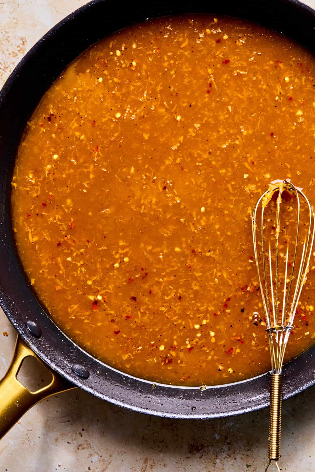 Spicy orange sauce in skillet with whisk before thickening.