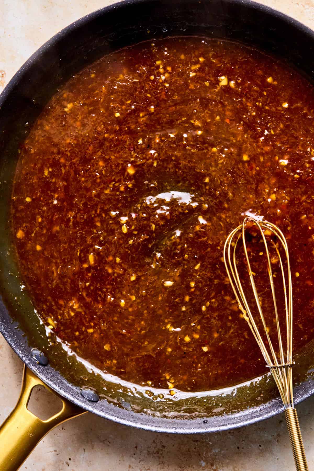 Cooked spicy orange sauce in skillet with whisk.