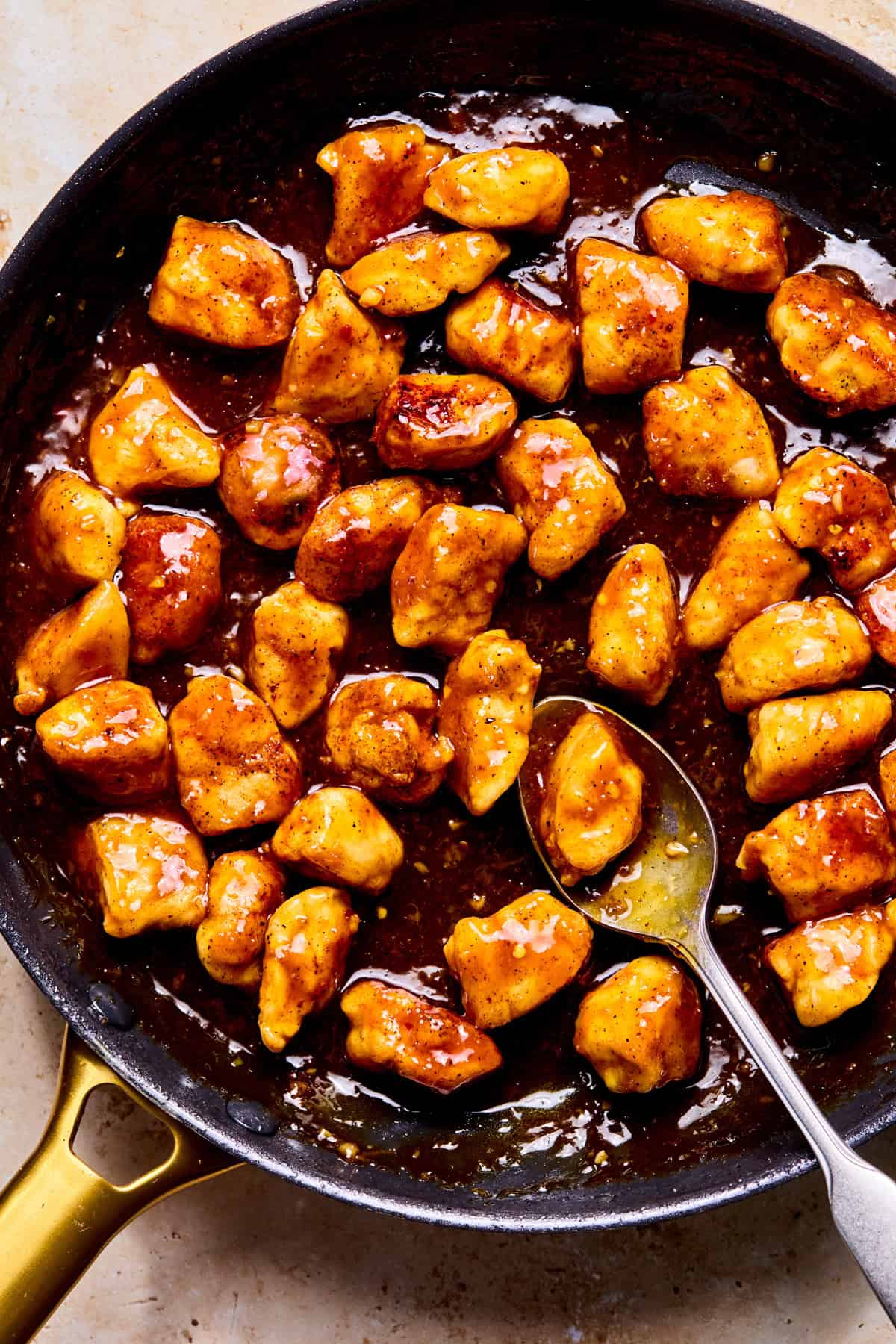 Spicy orange chicken in pan coated with sauce.